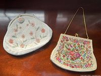 Two vintage evening bags on wooden surface, one white beaded and another embroidered with floral designs.