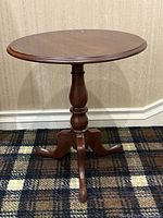 Front view of the walnut pedestal side table showing round top and carved three-legged base on patterned carpet.