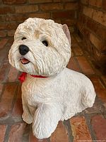 Front and slightly angled view showing textured white fur, black eyes, nose, pink tongue, and red ribbon on dog's neck.