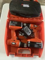 Photo showing two Black & Decker cordless drills with 18V batteries, charger, and branded tool bag inside an orange plastic carrying case.