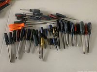 Overview of 30+ screwdrivers with mixed handle colors and sizes laid out on table.