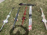 Five pairs of cross-country skis laid out on grass, four Atomic ARC skis and one Rossignol pair, alongside three sets of ski poles.