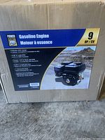Photo of the cardboard box showing brand Power Fist, 9 HP gasoline engine specifications and features such as 4-stroke OHV design, torque 14.07 ft-lbs at 500 RPM, 6 litre (1.6 gallon) gas tank, 1-inch horizontal shaft, and low oil shutdown.