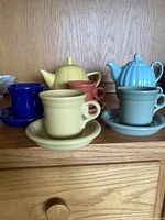 Photo of two ceramic teapots and four matching cups and saucers on wooden shelf.
