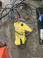 Top down view of the yellow K'Archor 210 power washer unit with cables and water inlet hose with orange connector attached.