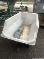Front-right side view of large white plastic dump cart with visible interior and wheels, showing light stains and rust marks inside basin.