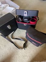 Three black camera cases arranged on carpet; cases are closed containing camera equipment inside; includes small black bag with red zipper pocket.
