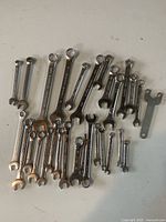 Over 20 mixed metal wrenches laid out on a white surface, showing different sizes and types including combination and open-end