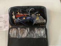 Photo of blue and orange Mastercraft multi cutter precision saw inside open black carrying case with power cord and six circular cutting blades wrapped in protective plastic sleeves.