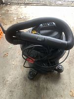 Front view showing black cylindrical Mastervac shop vacuum with flexible hose and power cord attached, positioned on four caster wheels.