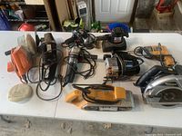 Overall view of the 9 power tools on a white folding table showing varied sizes and models in used condition.