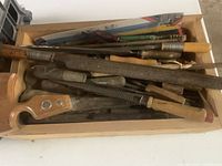 Full view of a wooden box with multiple metal files and a hand drill with wooden handle inside.