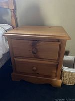 Front view of one solid pine bedside table with two drawers and wooden knobs.