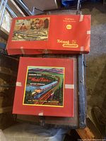 Two red cardboard boxes: top is Tri-ang Railways electric set box with family illustration and track; bottom is Standard Gauge Large Model Train Set battery operated box with diesel locomotive artwork