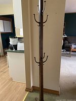 Full view of one vintage wooden coat rack in a living room setting, showing hooks and base.