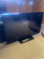 Full front view of Toshiba 40 inch flat screen TV on carpet with remote control on base.