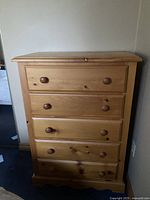 Front view of the pine tallboy dresser showing five drawers with wooden knob handles against a wall.