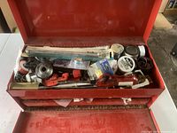 Top drawer of red metal toolbox showing plumbing tools, pipe cutter, Teflon tape, and metal fittings