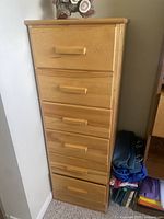 Front angled view of retro narrow solid wood dresser with five drawers and wooden pulls, showing surface wear marks on top.