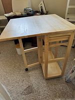 Folded table with one leg extended, showing the broad surface and open shelves beneath.