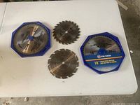 Four saw blades on white surface, two with packaging and two smaller unboxed blades.