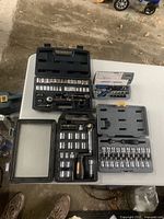 Overview of four plastic cases of socket sets laid out on white table with assorted ratchet handles and sockets visible