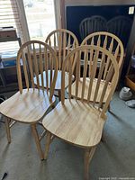 Four wooden dining room chairs grouped together showing front and side views, highlighting the spindle back design and contoured seats.