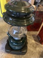 Photo of the green Coleman kerosene lantern showing metal top, glass globe, and control knob