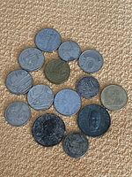 Collection of 15 various vintage coins laid on carpet, showing different sizes and colors.