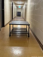 Full length view of the coffee table showing wood top and metal mesh shelf beneath on wheels, placed in hallway.