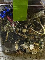 Close-up view of the jar tightly packed with various vintage jewelry pieces, showing blue beads, faux pearls, metal chains, and bracelets at the top.