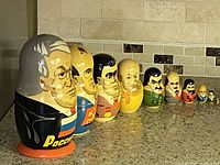 Photo showing the complete line-up of nine hand painted nesting dolls representing former Soviet leaders arranged from largest to smallest on a countertop.
