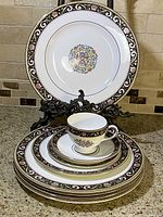 Photo of stack of plates, a cup, and a saucer with decorative brown floral border and floral medallion