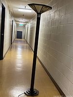 Full view of tall floor lamp off showing the entire lamp with stained glass shade and dark brass finish base in a hallway.