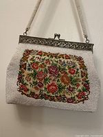 Front of the handbag showing the colorful floral petite point needlework surrounded by white beadwork, with the beaded strap visible.