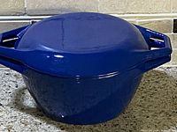 Top and side view of vintage navy blue enameled cast iron Dutch oven with lid in place on countertop.
