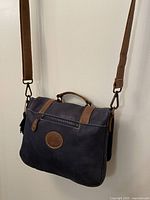 Front view showing navy blue leather with brown leather handle, strap, and front zipper pocket