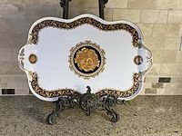 Full view of the white rectangular porcelain serving platter with double handles and ornate gold and navy blue decorations, displayed on a stand.
