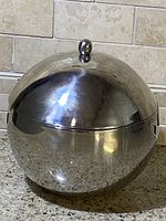 Closed vintage stainless steel ice bucket with dome lid and knob handle on countertop.