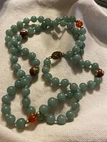 Full view of the jade bead necklace showing the green round beads, brown carved floral beads, and orange translucent beads with the sterling silver clasp visible.