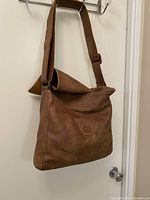 Front view of brown leather messenger bag hanging from hook
