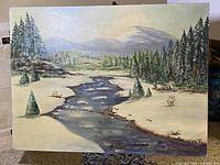 Full view of vintage winter landscape oil painting on canvas board showing river, snow, trees, and mountains.