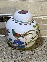 Porcelain ginger jar with lid on countertop, showing painted pheasant and flowers on jar body and lid