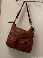 Front and side view of tan brown Roots leather shoulder bag hanging