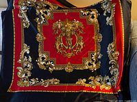 Full view of the square silk scarf showing an ornate gold and red baroque design on a black background.