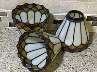 Close-up view of two stained glass lampshades placed side-by-side, focused on the alternating glass panel design and metal framing.