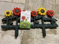 Full view of one fence panel featuring four sunflowers with attached packaging label showing an illustration of a fenced garden.