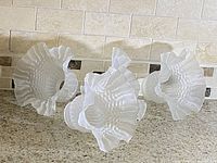 Set of 4 vintage frosted glass Victorian style light shades laid on countertop showing ruffled edges and textured body.