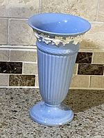 Full view of the Wedgwood light blue trumpet vase with embossed grapevine decoration on rim, showing overall condition and shape.