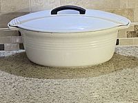 Side view of white oval Le Creuset Dutch oven showing shape, lid, handle, and general condition on kitchen countertop.